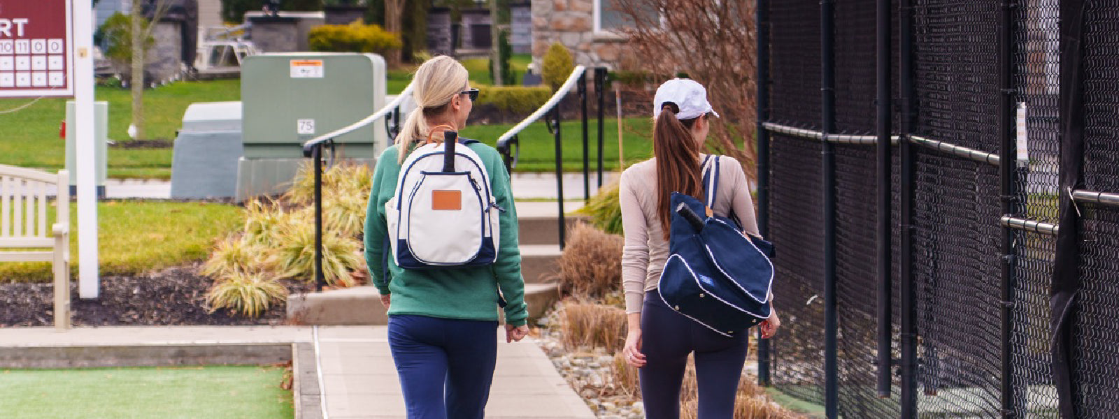 Two women leaving a pickleball court displaying pickleball products like bags, court towels and hats.