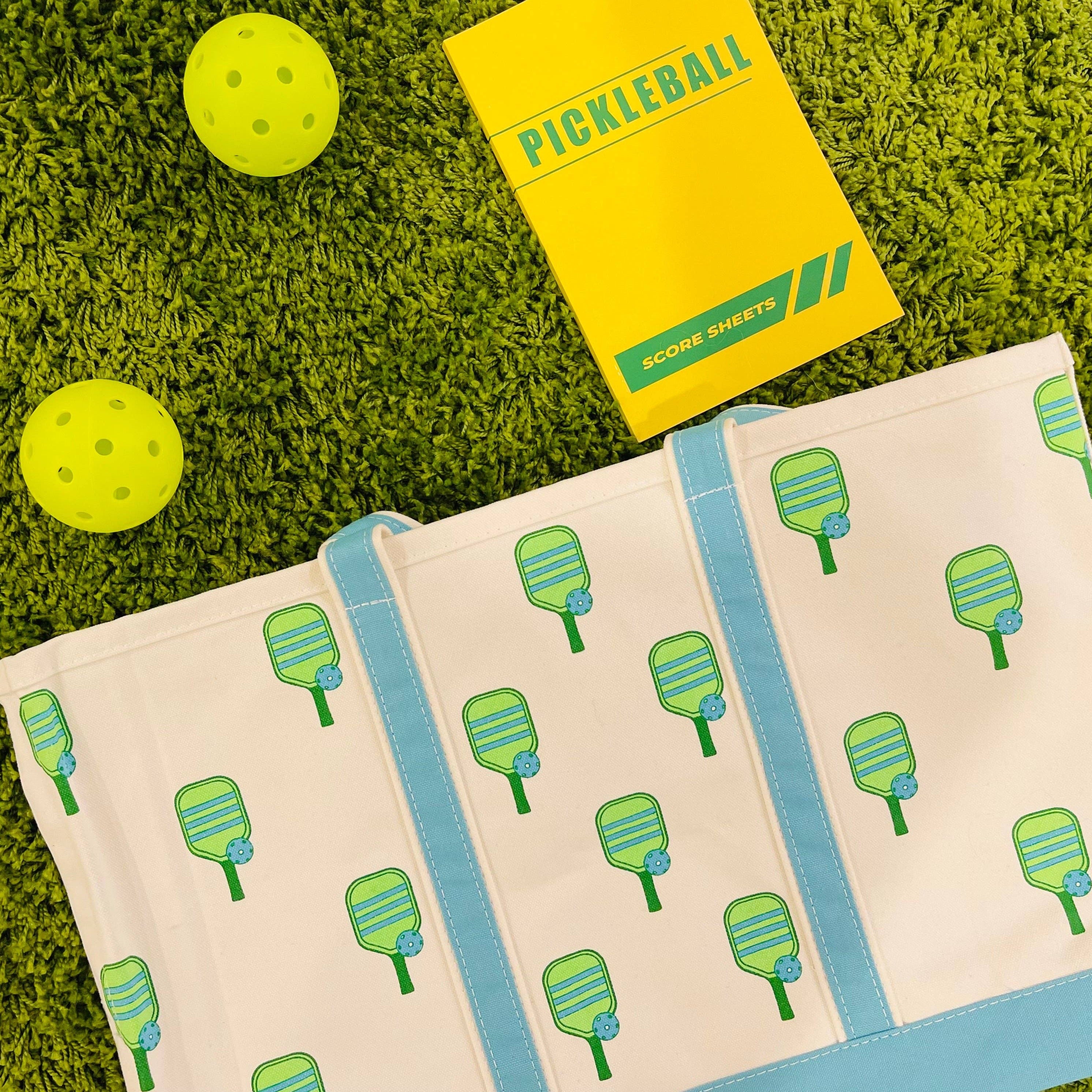 Pickleball paddle printed canvas tote bag laying in grass next to pickleballs