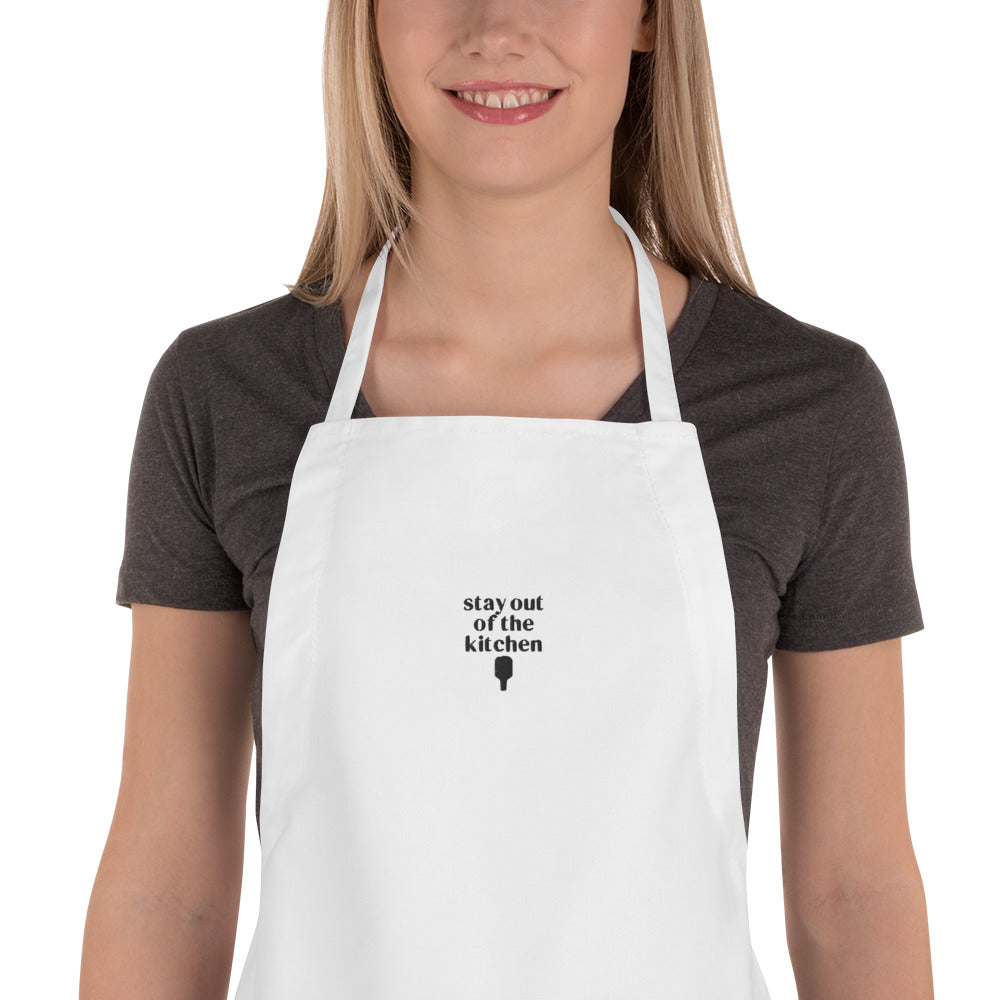 Detailed view of woman wearing an embroidered white apron that says "stay out of the kitchen" and has a pickleball paddle on it