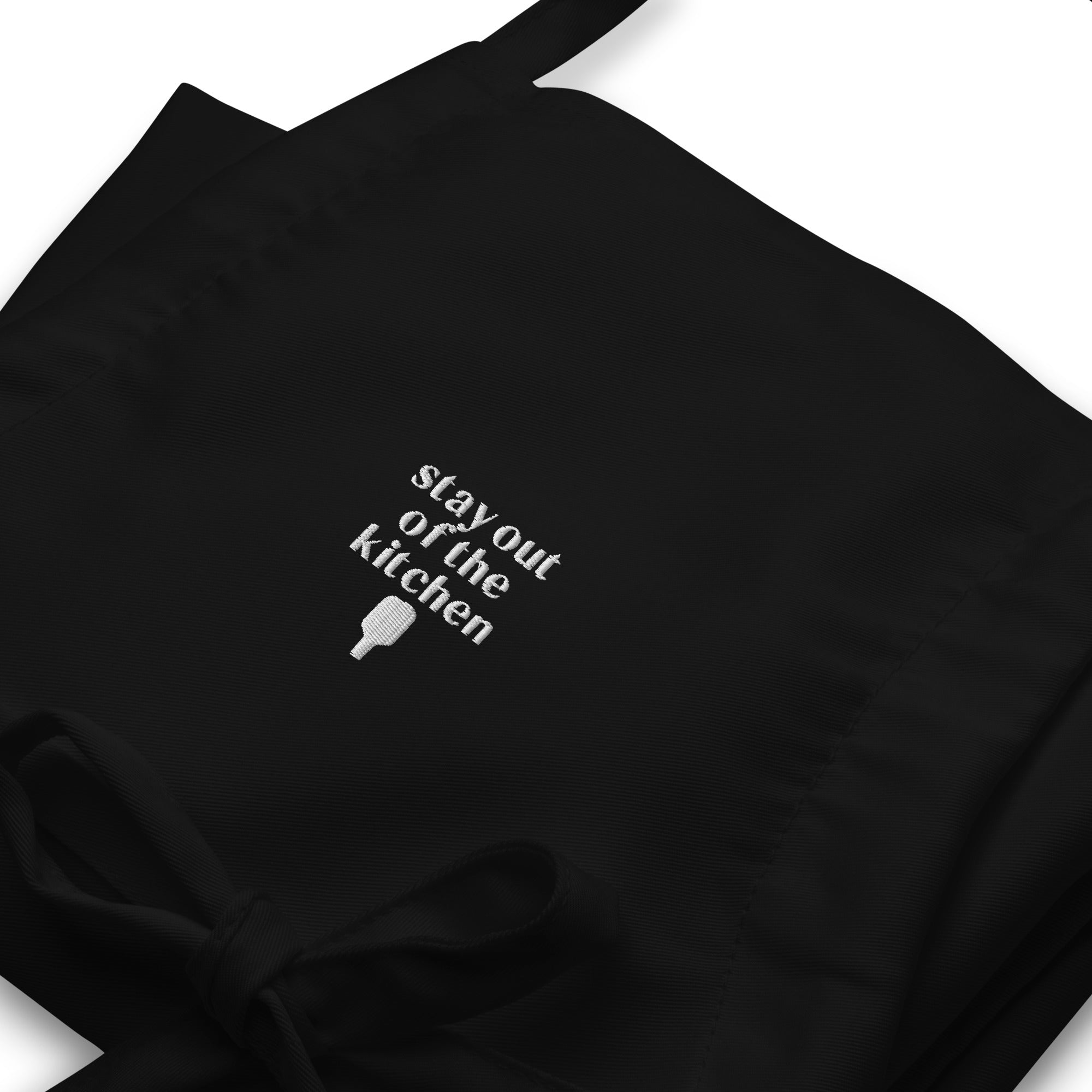 Detailed view of folded embroidered black apron that says "stay out of the kitchen" and has a pickleball paddle on it