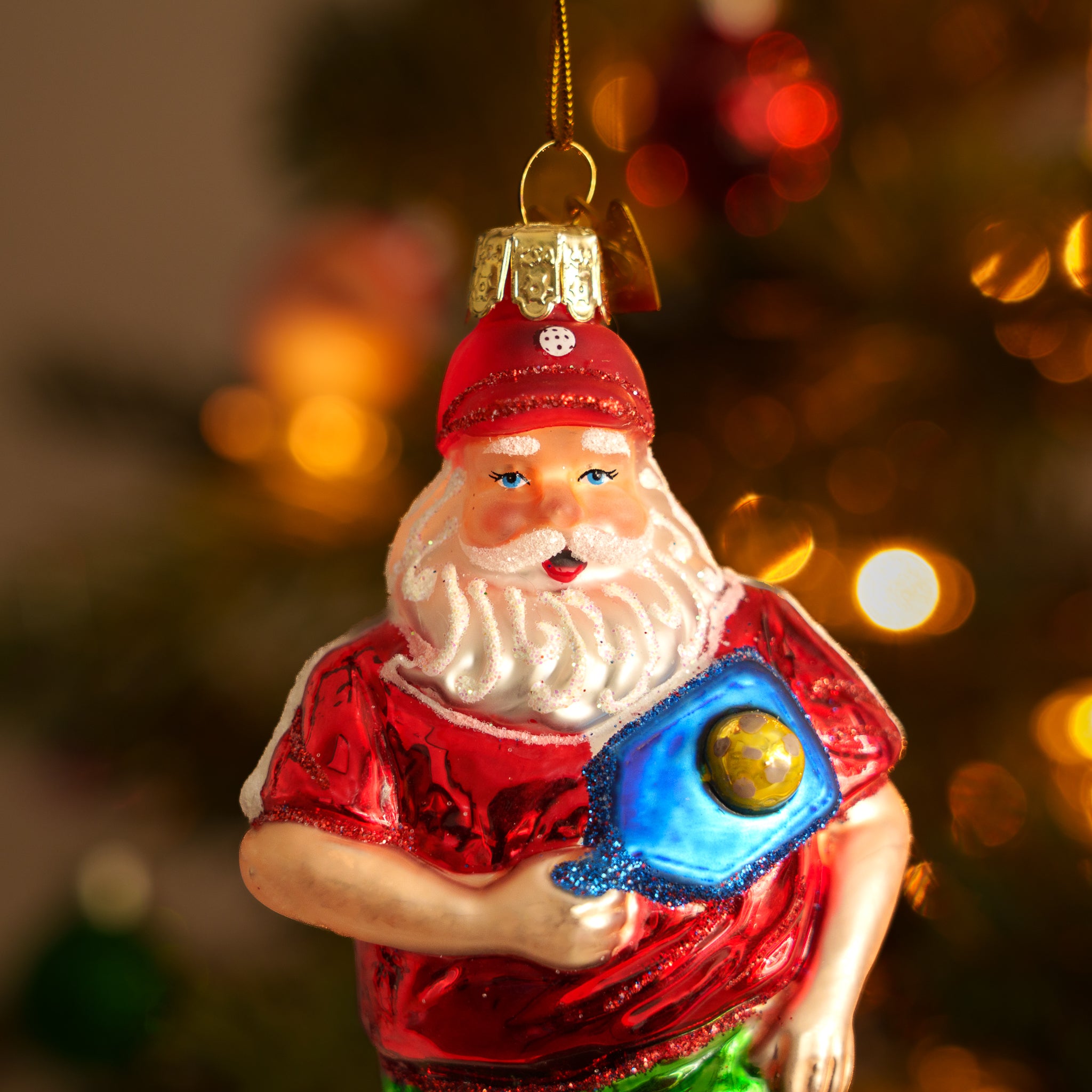 Close up of an elegant handmade glass Christmas ornament of Santa playing pickleball hanging on a Christmas tree