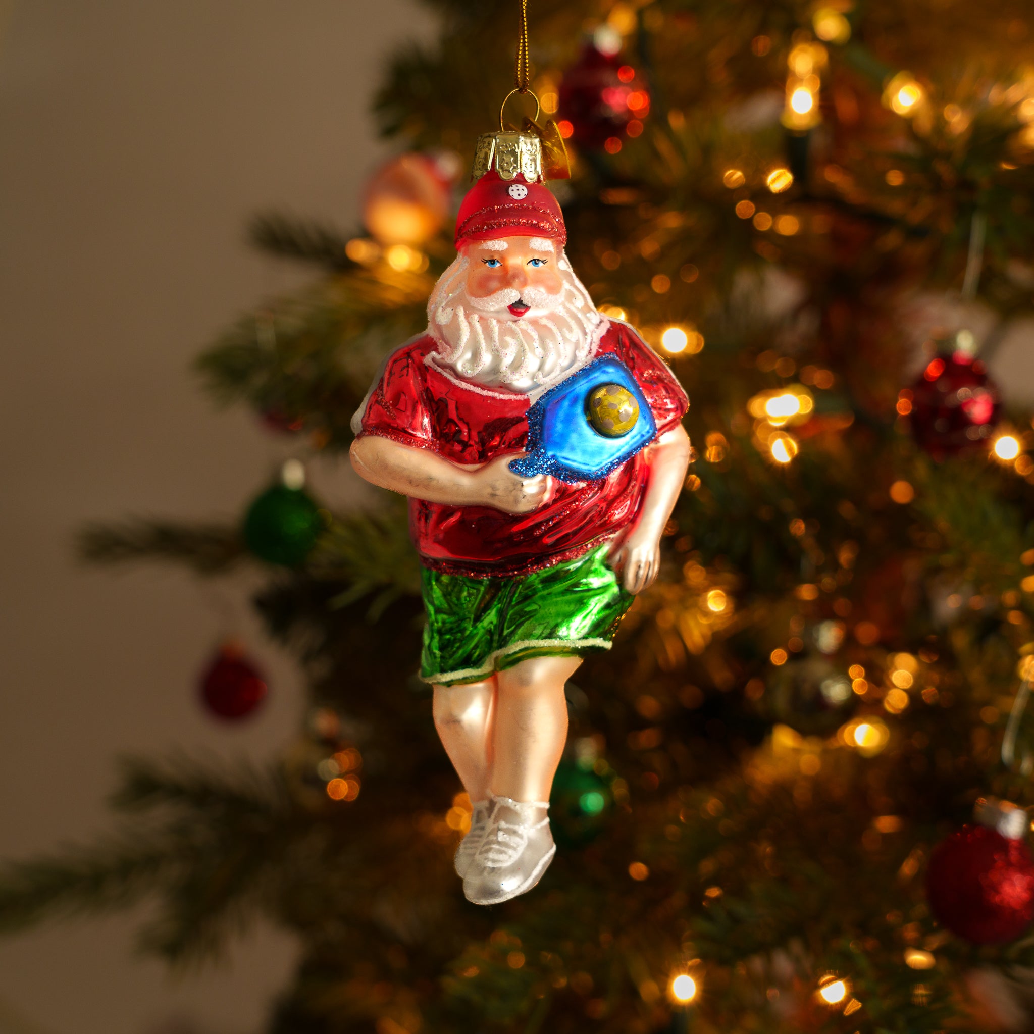 Elegant handmade glass Christmas ornament of Santa playing pickleball hanging on a Christmas tree