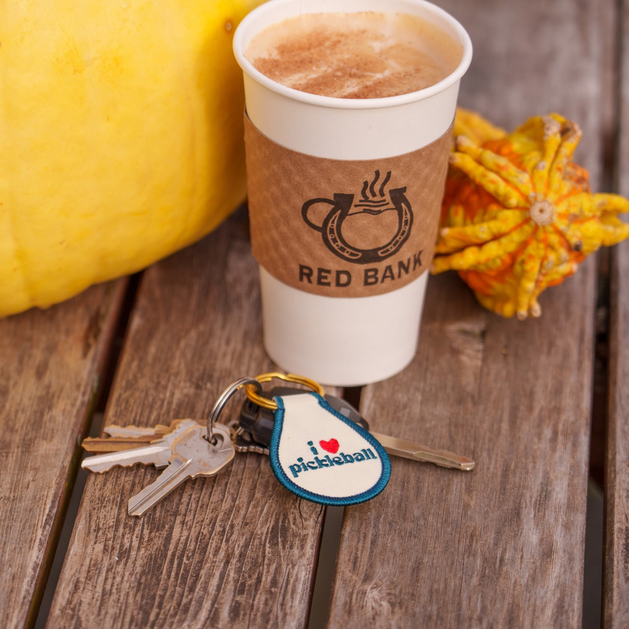 Keychain that says "I heart pickleball" on a table with keys, coffee and decorative fall gourds