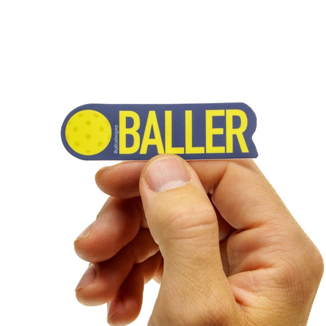 Sticker that has a pickleball and the words BALLER on it being held in hand