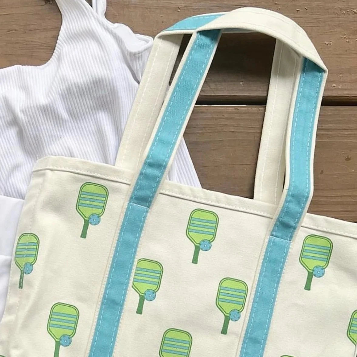 White canvas beach tote with blue handles and pickleball paddles laying flat on a table
