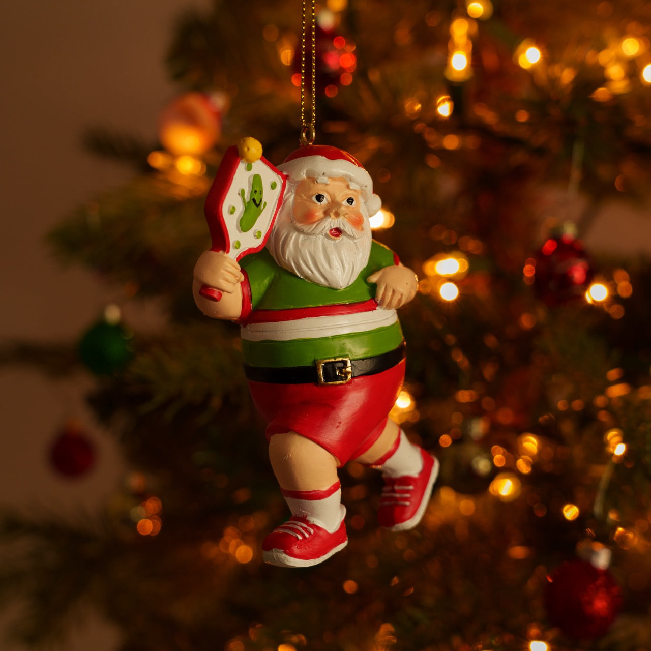 A colorful handmade resin Christmas tree ornament of Santa playing pickleball hanging on a Christmas tree