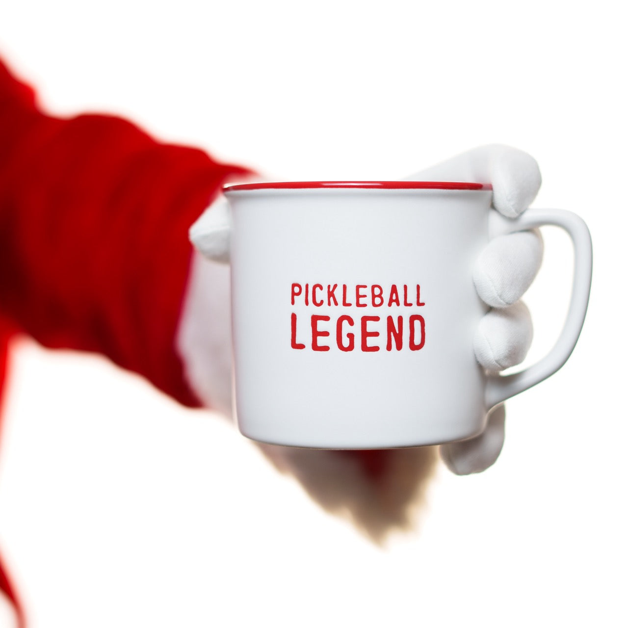 Santa holding a red and white ceramic coffee mug that says Pickleball Legend in red font in front of a white studio backdrop