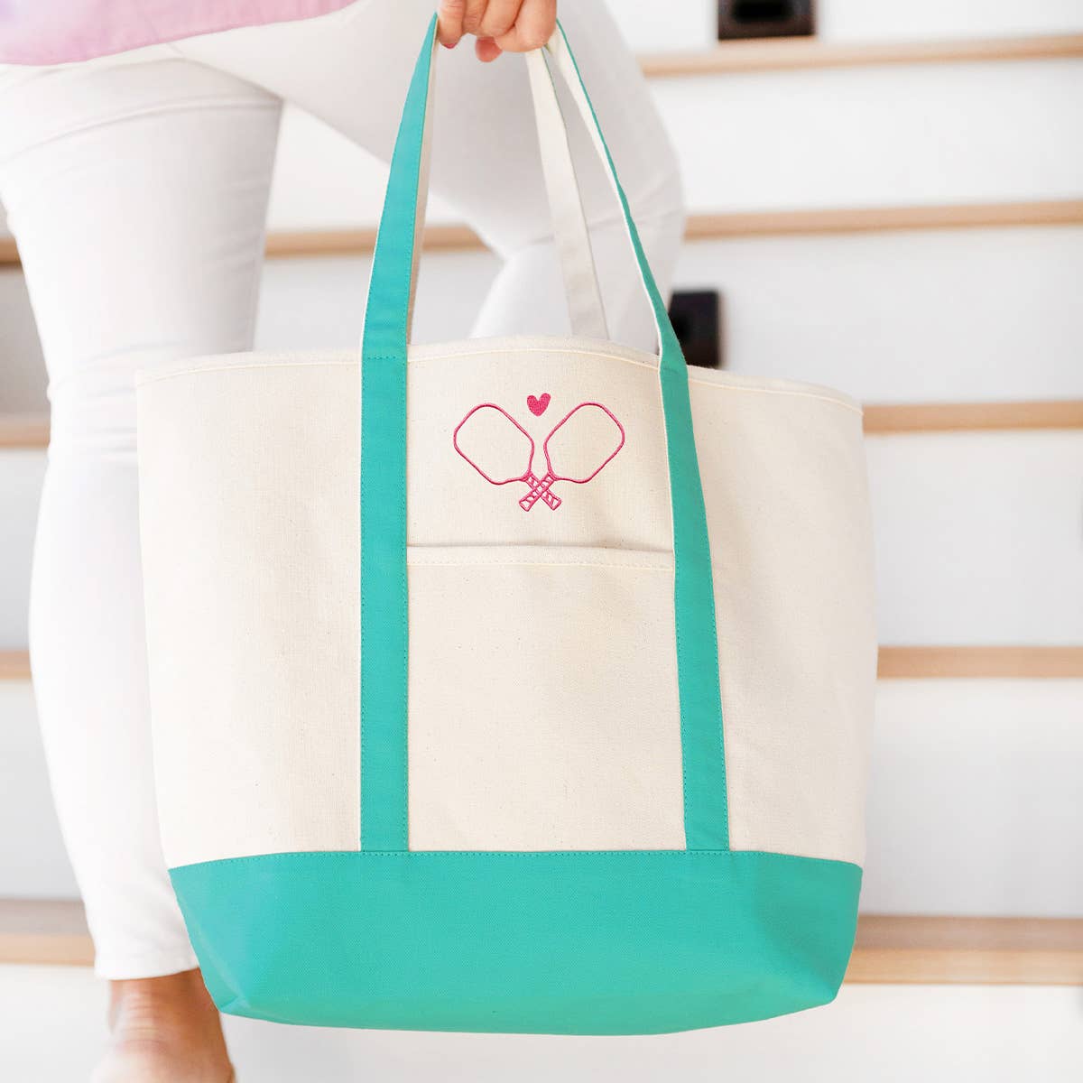 Canvas tote bag with pickleball paddles on it and teal colored accents being carried