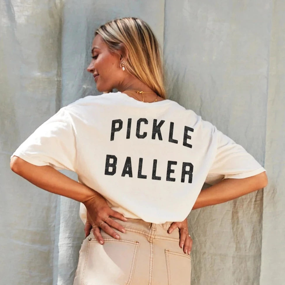 A woman wearing a cream tshirt that says "PICKLEBALLER" on the back