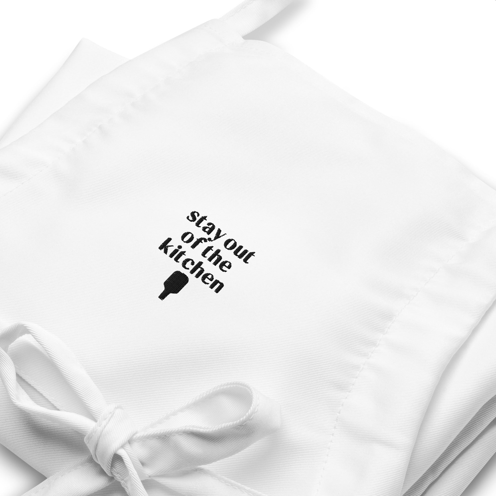 Detailed view of embroidered white apron that says "stay out of the kitchen" and has a pickleball paddle on it