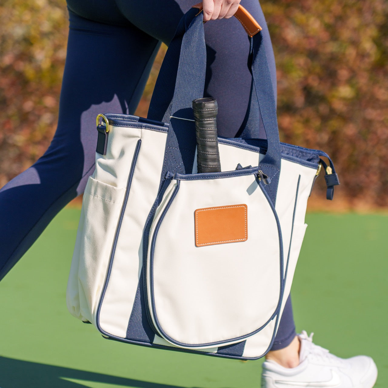 Person holding a white and navy pickleball tote bag with a pickleball paddle in it