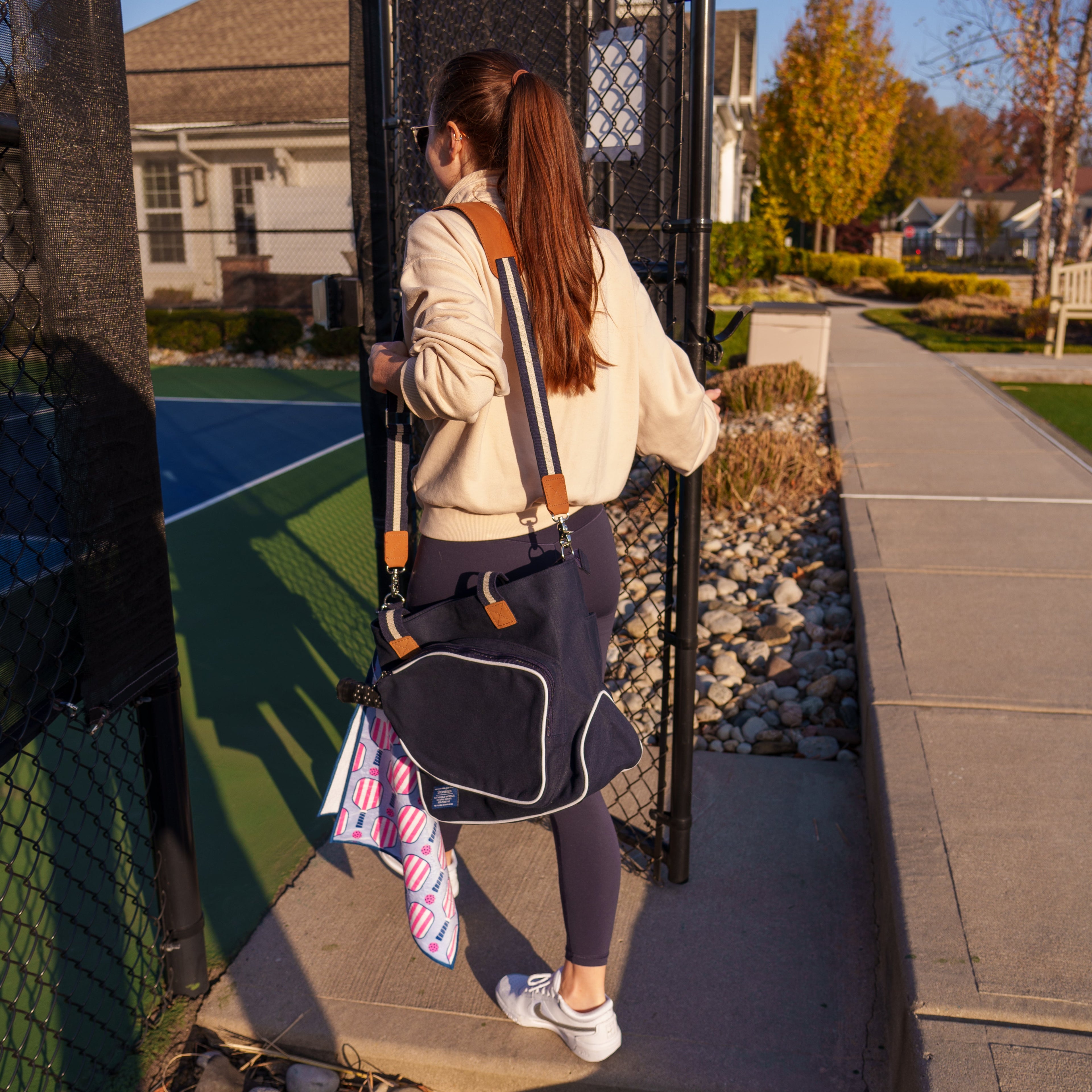 Woman walking onto a pickleball court with a pickleball tote bag and sports towel.