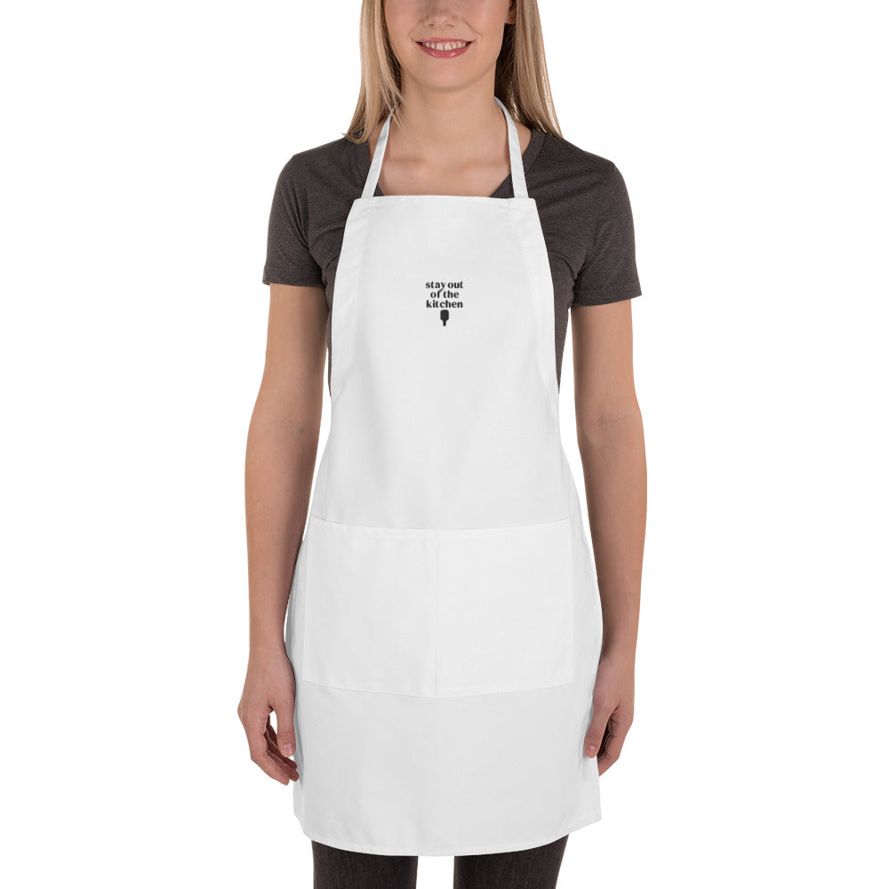 Woman wearing an embroidered white apron that says "stay out of the kitchen" and has a pickleball paddle on it