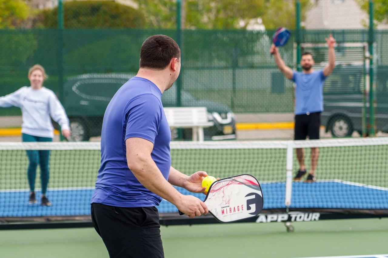 A pickleball player getting ready to serve to two players on the other side of the net