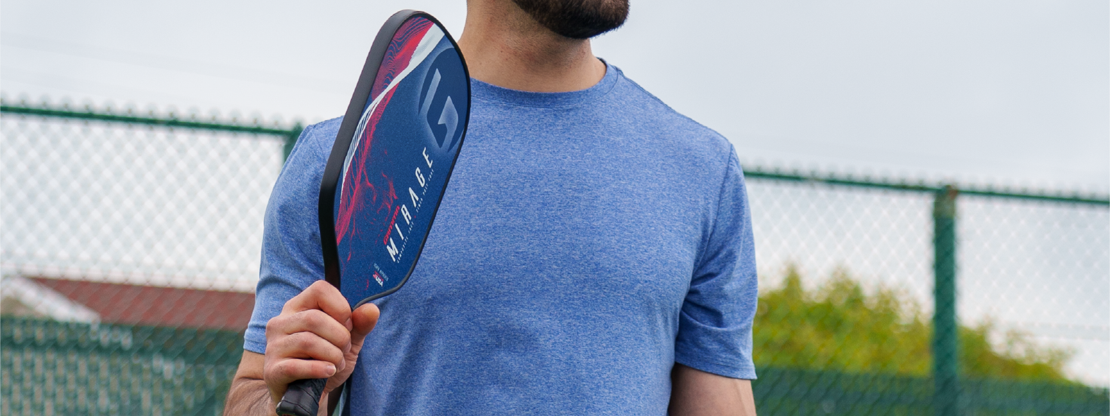 A man stands on a pickleball court with a pickleball paddle in his hand preparing to serve the ball.