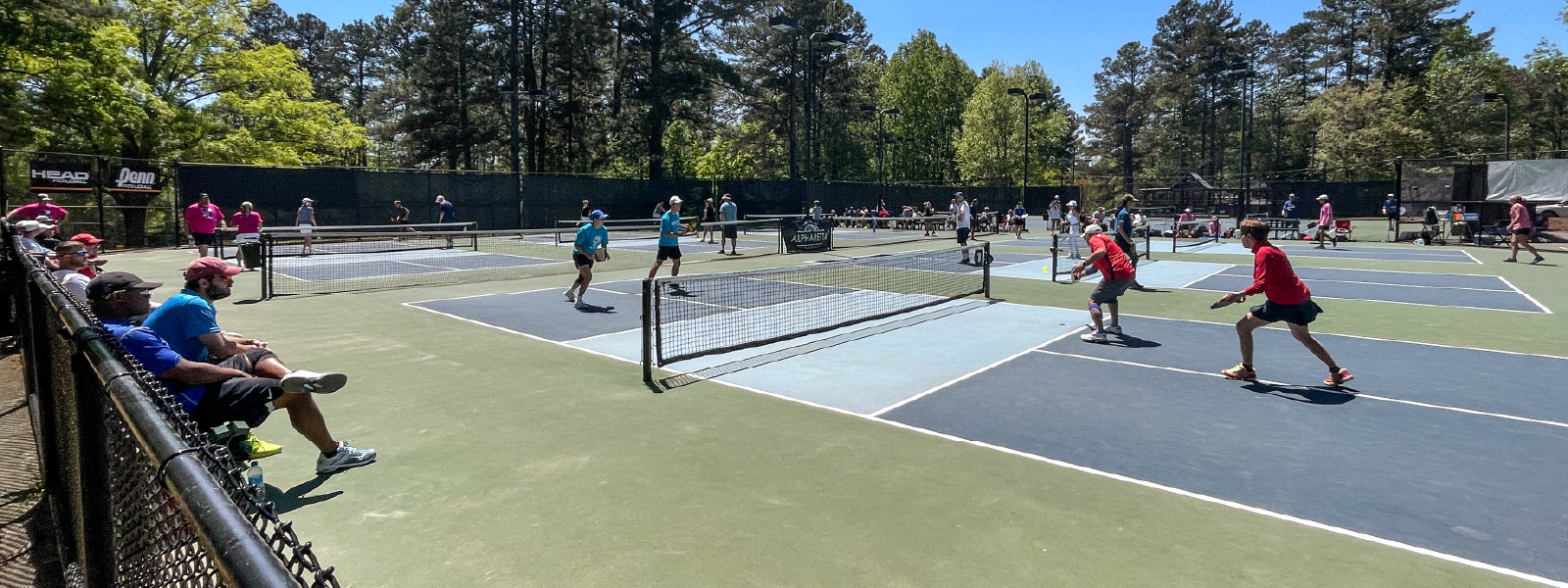 Group of retired pickleball players on a court playing doubles on a sunny day.