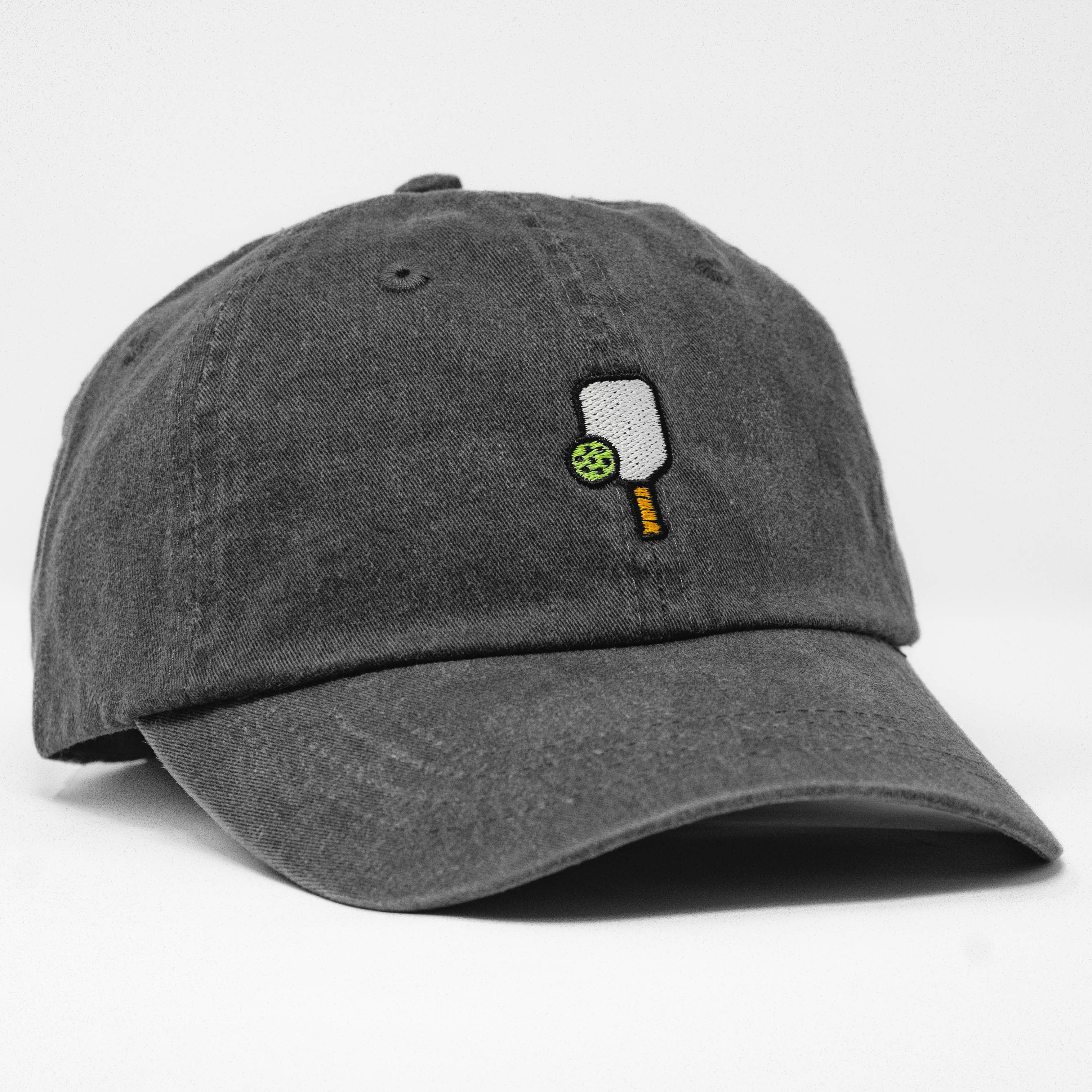 Side of washed black baseball hat that has an embroidered pickleball paddle and ball on it