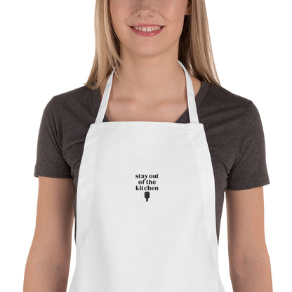Detailed view of woman wearing an embroidered white apron that says &quot;stay out of the kitchen&quot; and has a pickleball paddle on it
