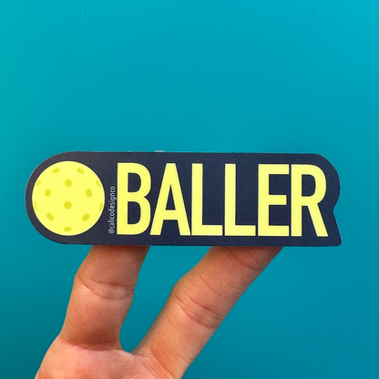 Sticker that has a pickleball and the words BALLER on it being held