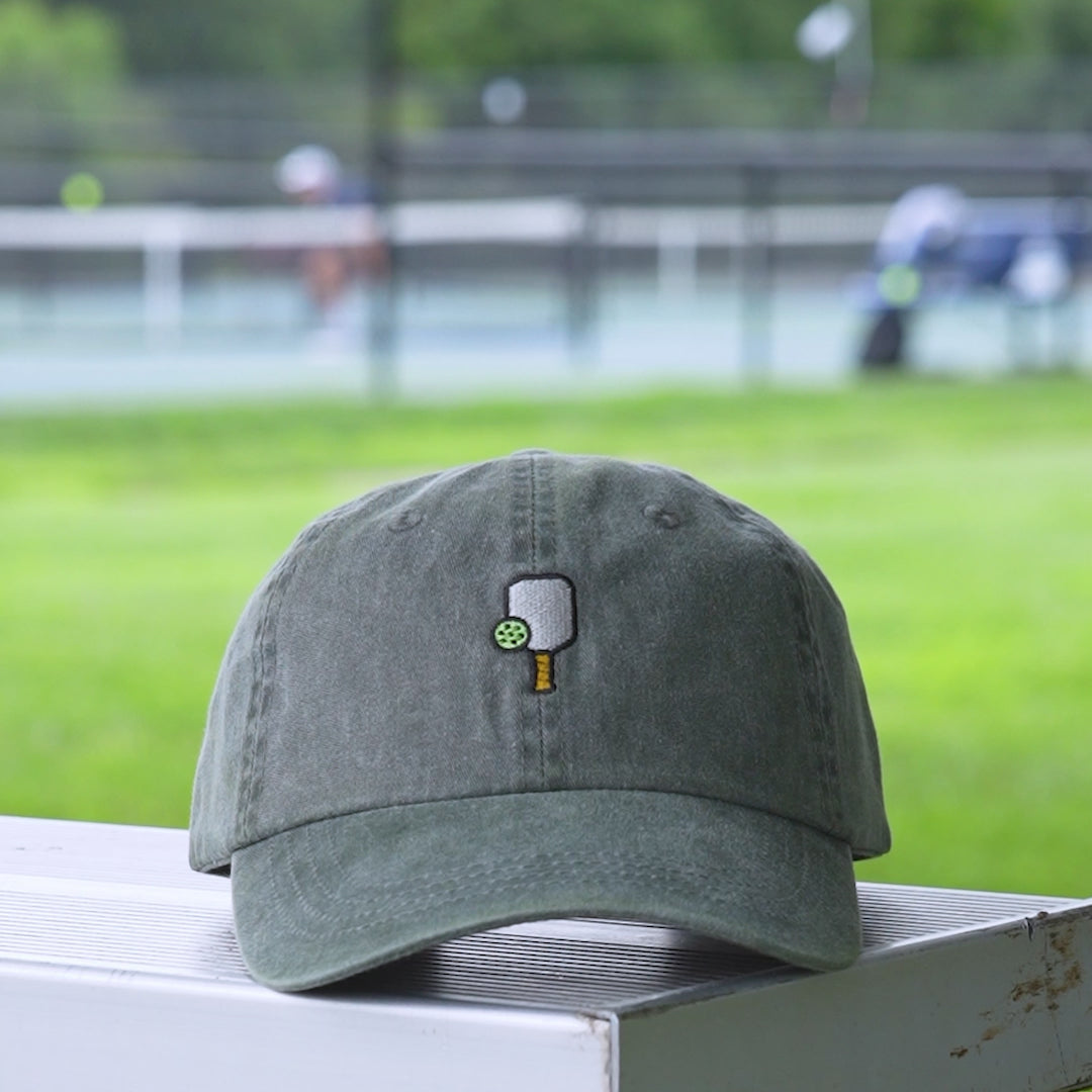 Video of a washed green baseball hat with an embroidered pickleball  and pickleball paddle on it.