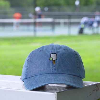Video of a washed denim baseball hat with an embroidered pickleball  and pickleball paddle on it.