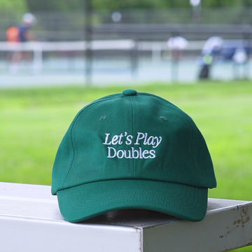 Video of a green baseball hat with embroidered white words says Lets Play Doubles on it.