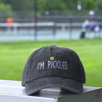 Video of a washed black baseball hat with an embroidered pickleball and white words saying IM PICKLED on it.