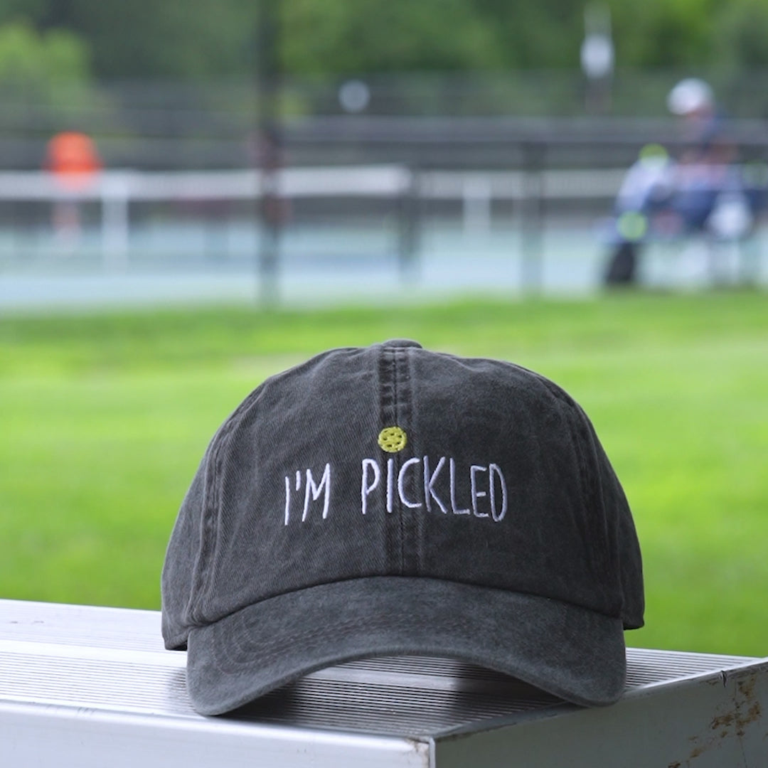Video of a washed black baseball hat with an embroidered pickleball and white words saying IM PICKLED on it.