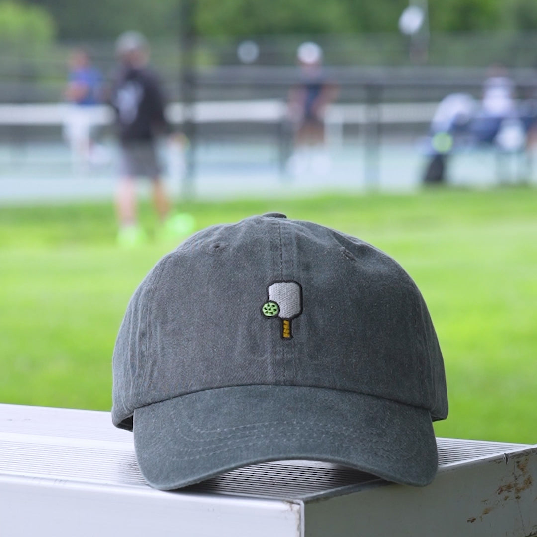 Video of a washed black baseball hat with an embroidered pickleball  and pickleball paddle on it.