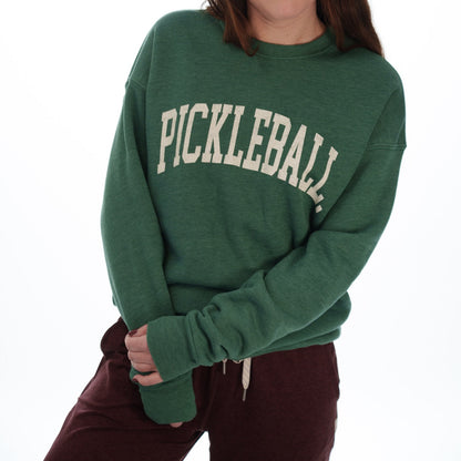 Woman wearing maroon pants and a green crewneck sweatshirt that says &quot;PICKLEBALL&quot; on it in white lettering