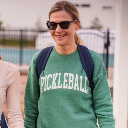 Woman wearing a green crewneck sweatshirt that says &quot;PICKLEBALL&quot; on it